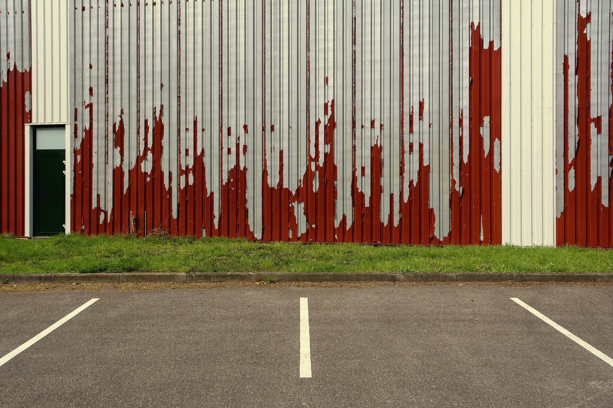A long ribbed metal exterior wall in weathered red, the kind of run continuous gutter is fabricated to match
