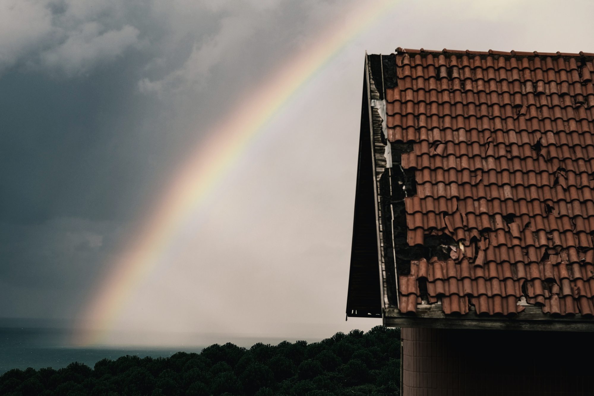 A hail-struck tile roof with shattered courses under a breaking storm sky