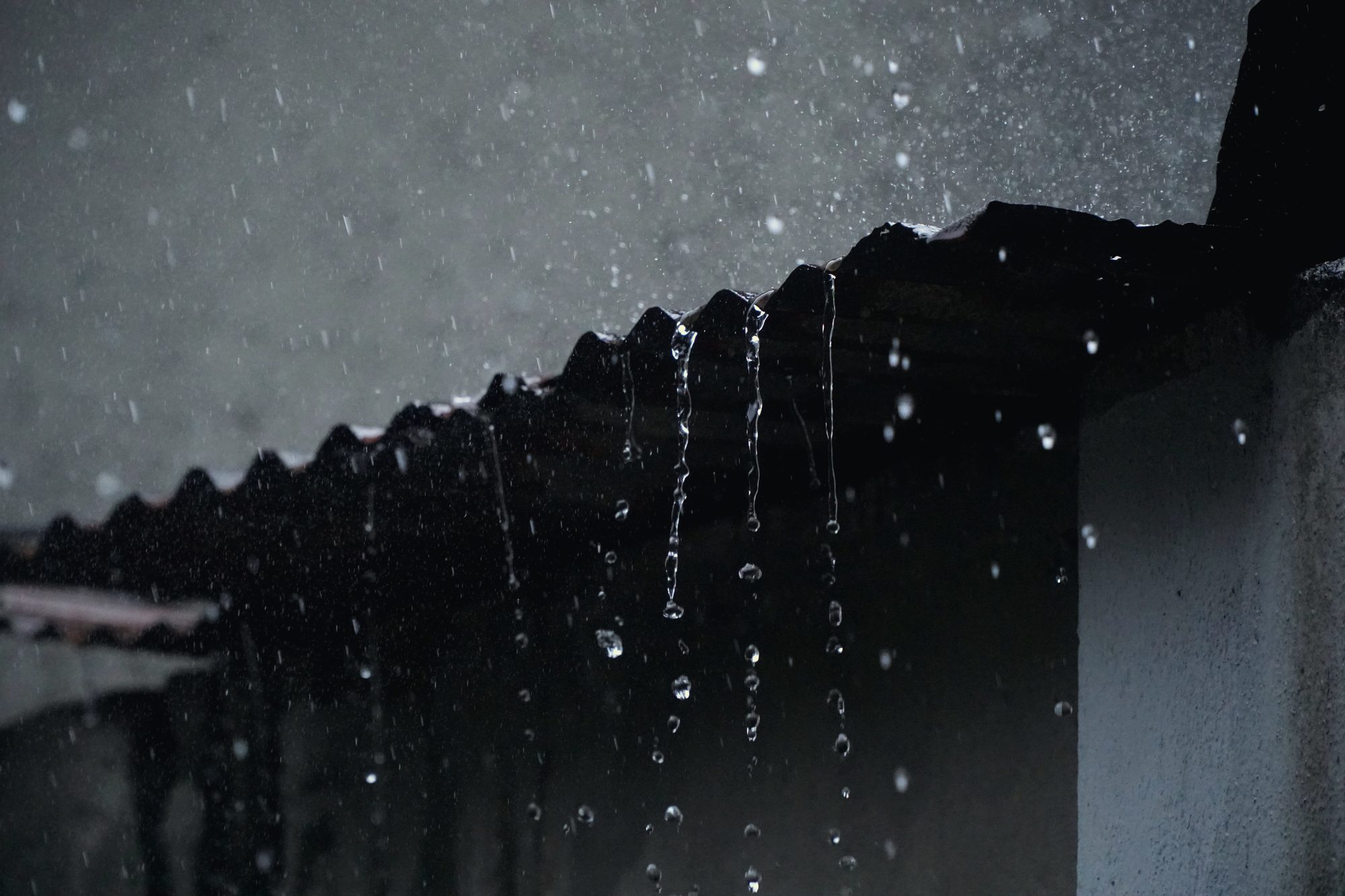 Rain sheeting off the edge of a roof at dusk, the kind of night that fills our phone
